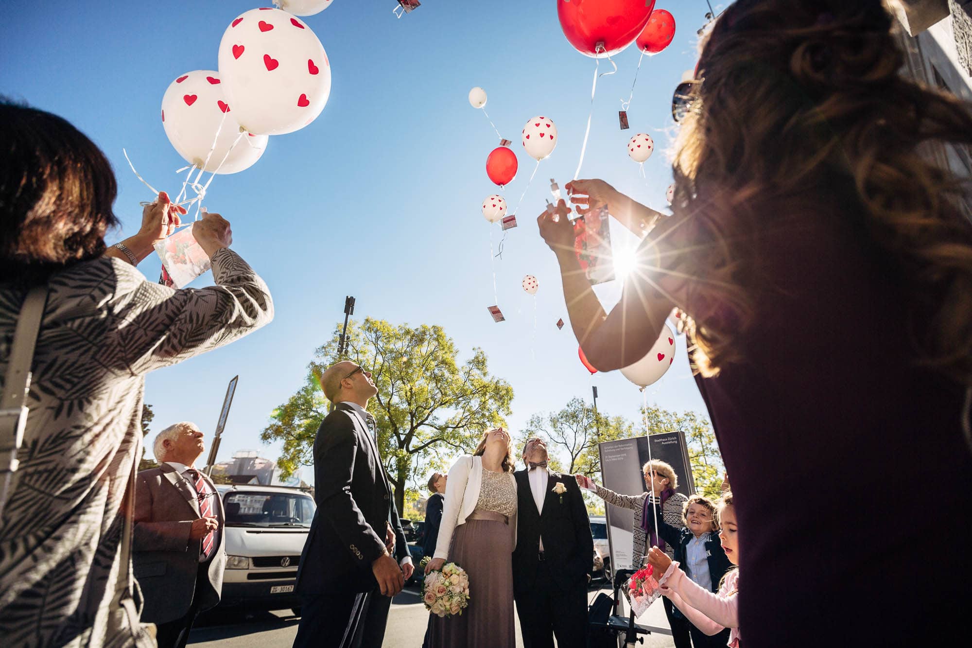 Gäste und Brautpaar lassen Ballone steigen. Sonne als Gegenlicht
