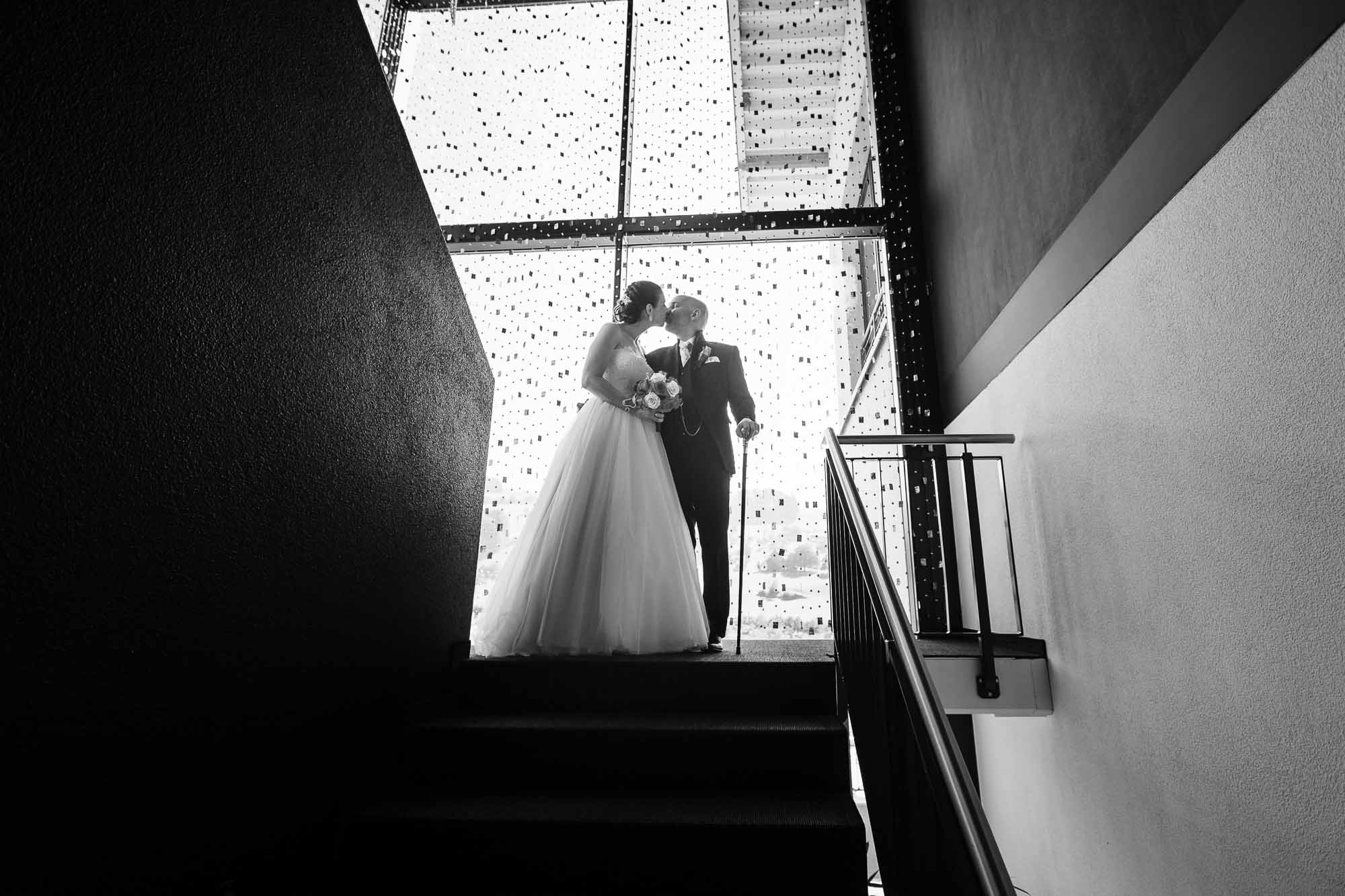 Brautpaar küsst sich im Treppenhaus vor Fenster