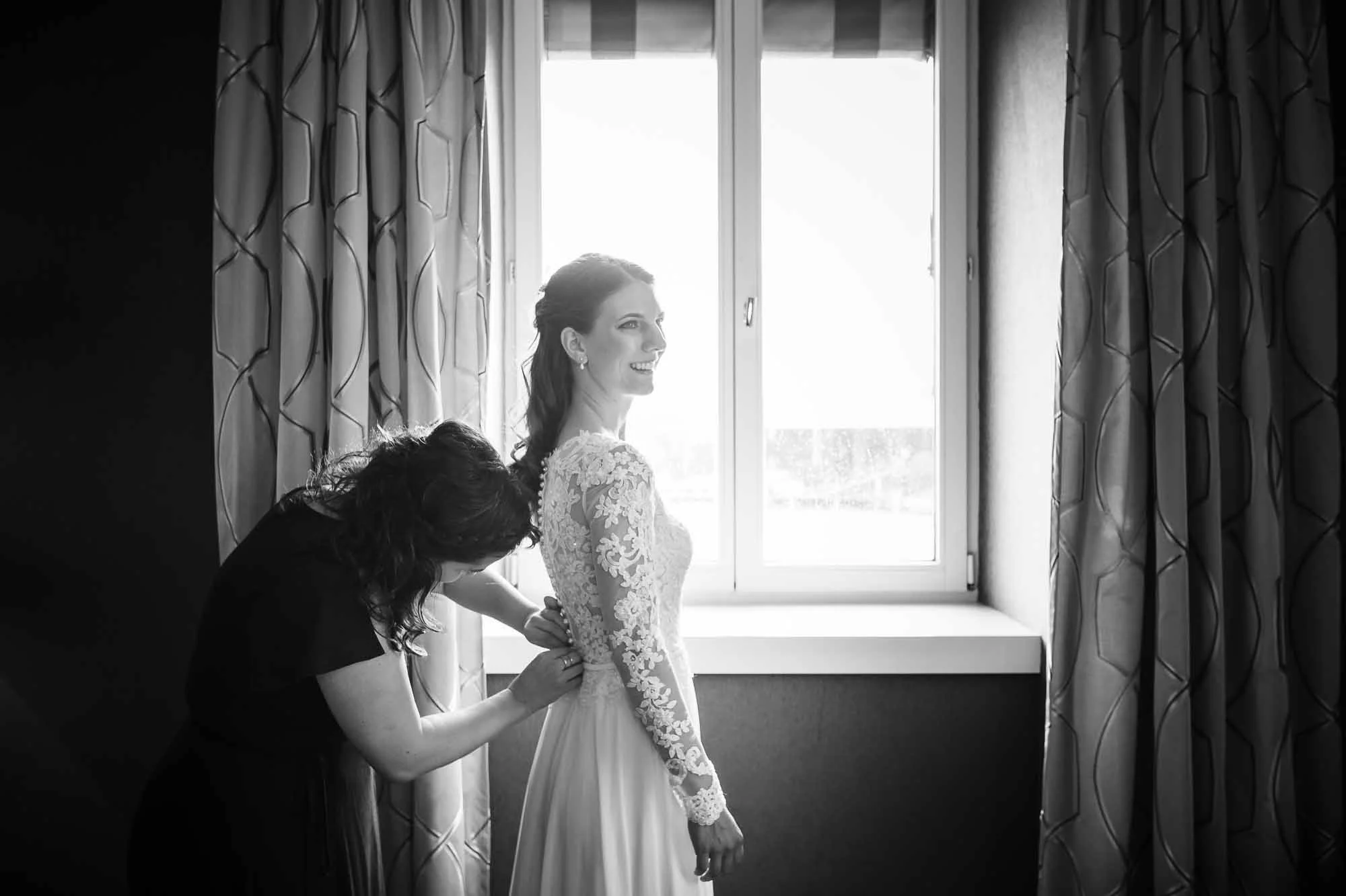 Braut wird angezogen vor Fenster Hochzeitsbilder Luzern