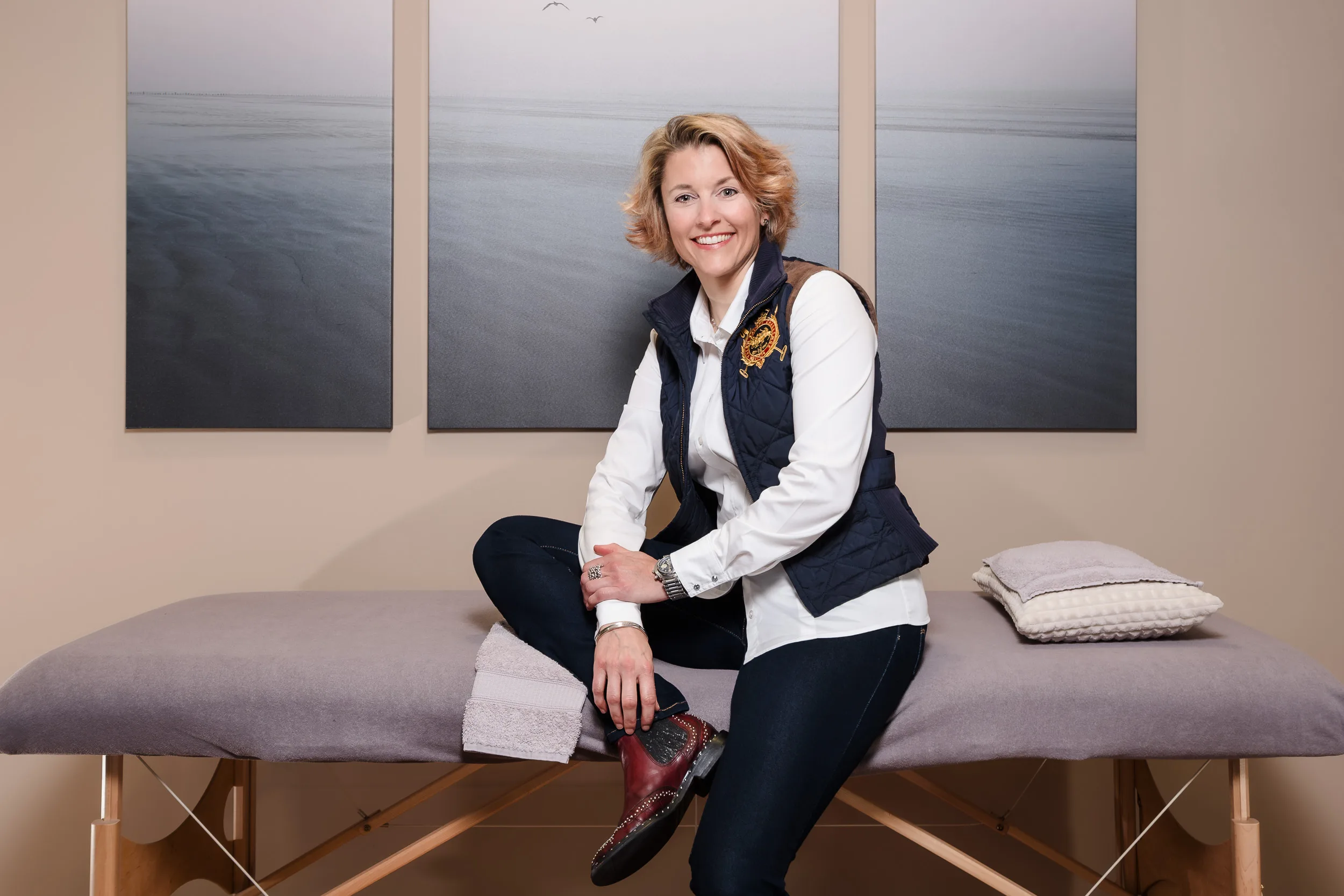 Frau sitzend auf Massagetisch schaut freundliche in die Kamera.